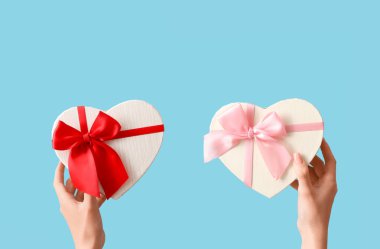 Mavi arka planda kalp şeklinde hediye kutuları olan kadın eller. Sevgililer Günü kutlaması