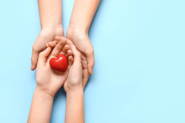 Mavi arka planda kırmızı kalp tutan kadın ve çocuğun elleri