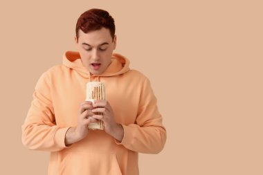 Genç ve şaşkın adam bej arka planda lezzetli bir donör kebabı tutuyor.