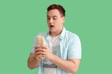 Genç ve şaşkın bir adam yeşil arka planda donör kebabı tutuyor.