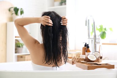 Güzel genç bir kadın banyoda hindistan cevizli saç maskesi takıyor.