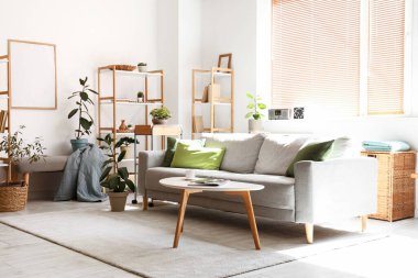 Gri kanepesi, çiçekleri, sehpası ve raf ünitesi olan şık bir oturma odası.