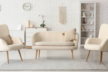 Beyaz tuğla duvara karşı kanepe ve koltuklu oturma odasının içinde.