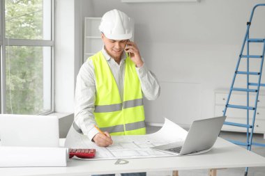 Erkek müteahhit odada cep telefonuyla konuşuyor.