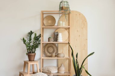 Odada beyaz duvarın yanında heykelcikli raflar ve bitkiler var.