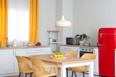 Beyaz tezgahlı modern mutfak, yemek masası, kırmızı buzdolabı, sandalyeler ve lamba.