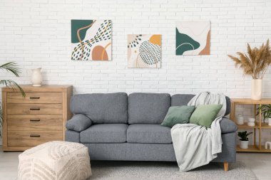 İçinde rahat bir kanepe, puf, çekmeceler ve resimler olan güzel bir oturma odası.