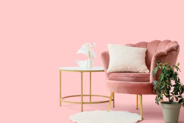 Ev bitkisi, kahve masası ve pembe arka planda halı olan güzel bir koltuk.