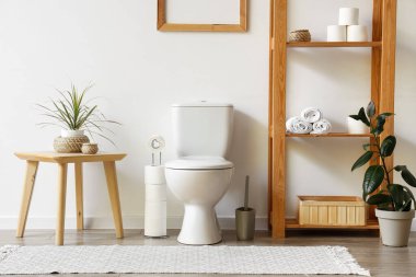 Tuvaletin içinde klozet, sehpa ve raflar beyaz duvarın yanında.