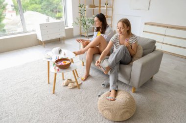 Ojeli genç kadınlar oturma odasında pedikür yapıyor.