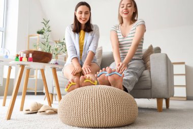 Ayak parmaklarını ayıran genç kadınlar oturma odasında pedikür yapıyorlar.