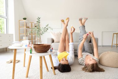 Ayak parmaklarını ayıran genç kadınlar oturma odasında pedikür yapıyorlar.