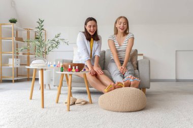 Ojeli genç kadınlar oturma odasında pedikür yapıyor.