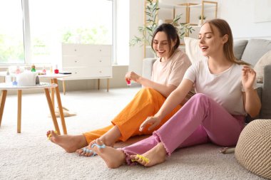 Ayak parmaklarını ayıran genç kadınlar oturma odasında pedikür yapıyorlar.