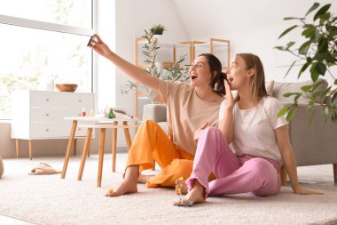 Genç kadınlar pedikür yapıyor ve oturma odasında selfie çekiyor.