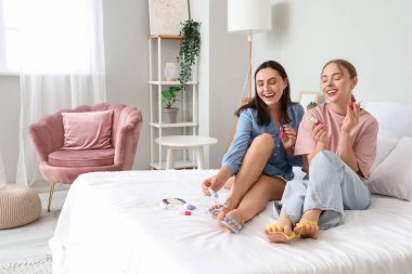 Ayak parmağı ayırıcı ve ojeli genç kadınlar yatak odasında pedikür yapıyor.