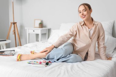 Yatak odasında pedikür için ayak parmağı ayırıcı kullanan genç bir kadın.