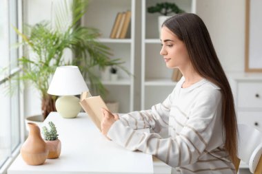 Oturma odasında kitap okuyan güzel genç bir kadın.