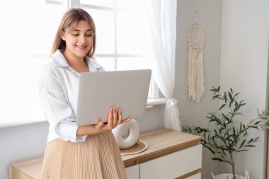 Evde dizüstü bilgisayar kullanan genç bir kadın.