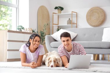 Evde dizüstü bilgisayar kullanan sevimli köpekli genç bir çift.