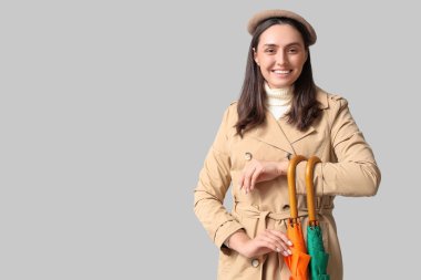 Gri arka planda şemsiyeleri olan mutlu genç bir kadın.