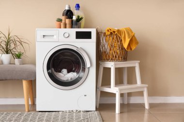 Modern çamaşır makinesi, yedek kulübesi ve sepeti bej duvarın yanında.