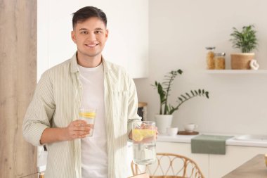 Elinde sürahi ve bir bardak limonlu su olan genç adam mutfakta.
