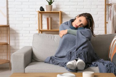 Oturma odasındaki kanepede ekoseye sarılı depresyondaki genç kadın.