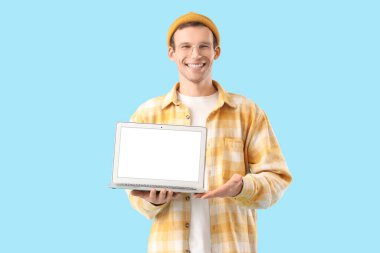 Mavi arka planda boş dizüstü bilgisayarı olan genç bir adam.