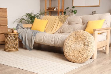 Aydınlık oturma odasının içinde bej renkli kanepe, masa ve puf