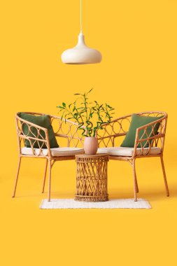 Vazoda bambu saplı masa, sarı arka planda koltuklar ve lamba.