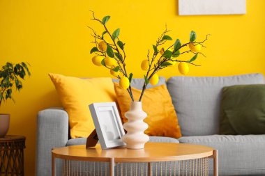 Oturma odasındaki masada ağaç dalları, limonlar ve çerçeveli vazo.