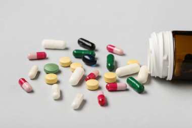 Gri arka planda farklı haplar içeren şişe, yakın plan.