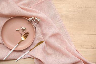 Ahşap arka planda çatal bıçak, peçete ve çigila çiçekli tabak.