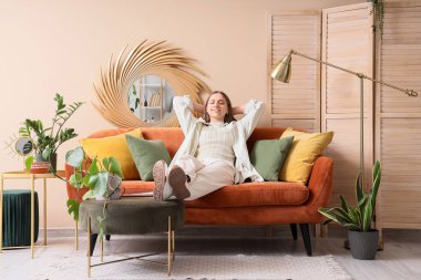 Oturma odasındaki rahat kahverengi kanepede oturan genç kadın.