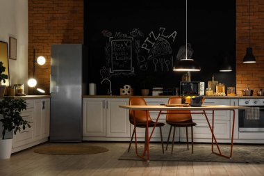 Tezgahları, yemek masası ve geceleri parlayan lambaları olan şık bir mutfak.