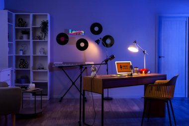 Karanlık podcaster stüdyosunun içinde iş yeri, vinil diskler ve parlayan lambalar var.
