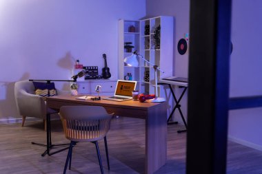 Podcaster 'ın atölyesinin içinde çalışma yeri, koltuk ve parlayan lamba var.