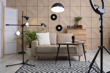 Podcaster 'ın stüdyosunun içinde kanepe, masa ve parlayan lambalar var.