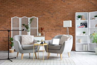 Podcaster 'ın stüdyosunun içinde koltuklar, katlanır ekran ve raf ünitesi