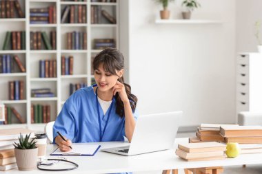 Kütüphanedeki masada çalışan kadın stajyer doktor.