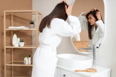 Banyoda aynanın yanında saç dökülmesi sorunu olan endişeli genç bir kadın.