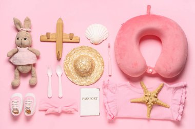 Çocuk kıyafetleri, pasaport ve pembe arka planda oyuncakları olan kompozisyon