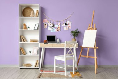 Çalışma masası sehpası, raf ünitesi ve modern dizüstü bilgisayarla birlikte odada menekşe duvarın yanında.