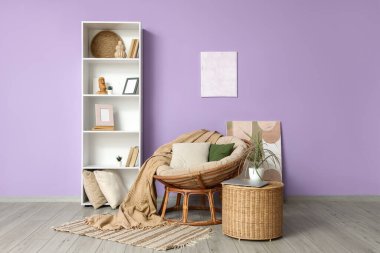 Odanın içinde, menekşe duvarın yanında rahat bir koltuk, masa ve raf var.