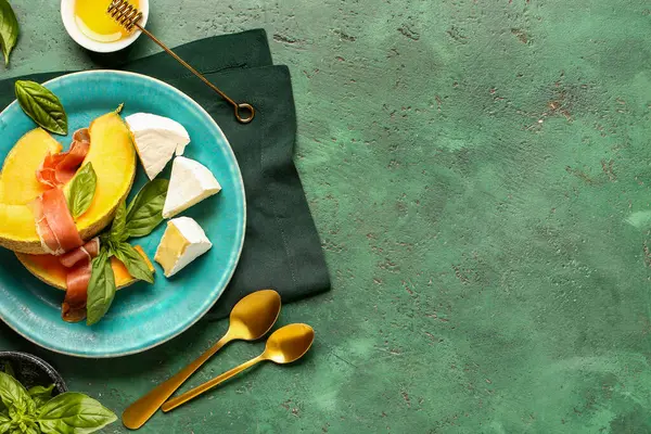 Yeşil arka planda lezzetli kavun, jambon, peynir ve fesleğen tabağı.