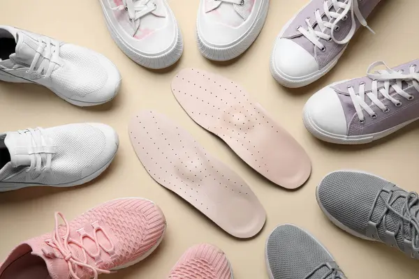 Bej arka planda farklı spor ayakkabıları ve ortopedik tabanlı kompozisyon