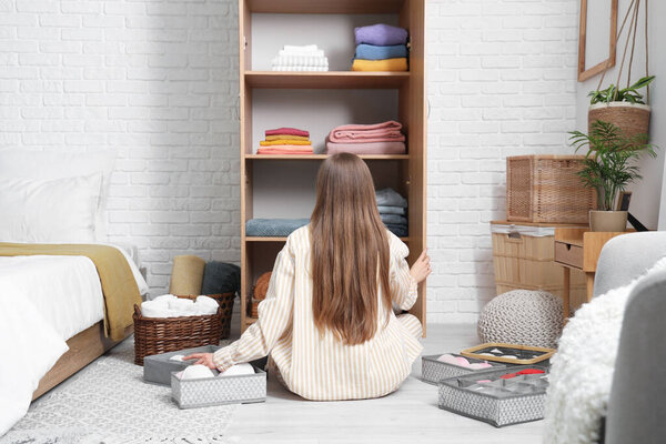 Молодая женщина складывает чистую одежду в шкаф