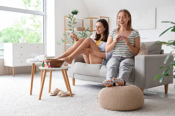 Ojeli genç kadınlar oturma odasında pedikür yapıyor.