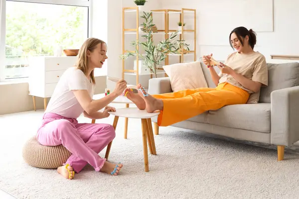 Posta cilası sürmüş genç kadınlar oturma odasında pedikür yapıyor.